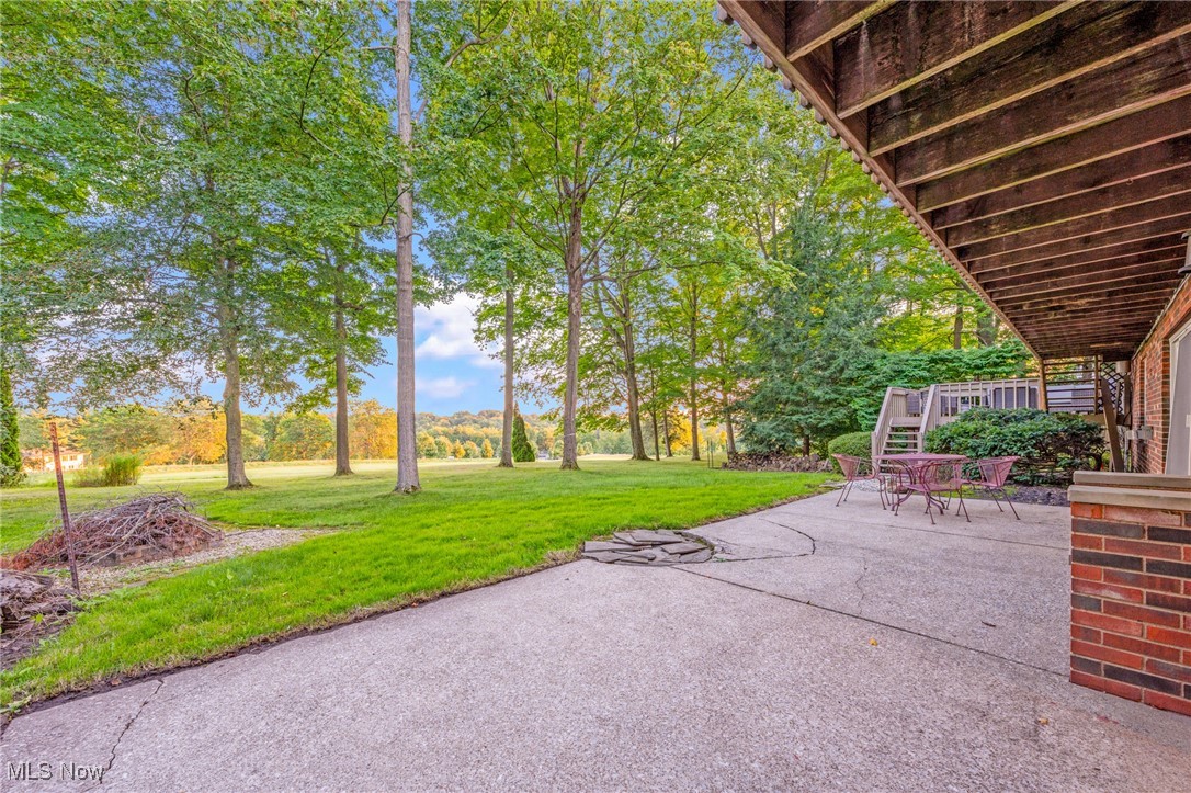 Covered patio with outdoor table and chairs overlooking a tree-lined lawn and open field.