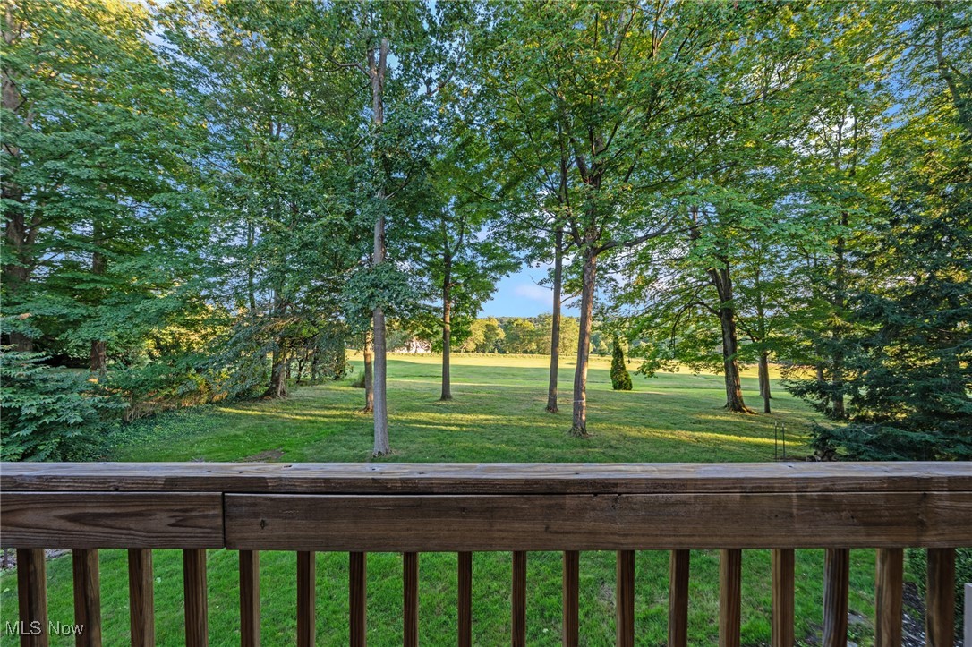 Tree-framed lawn and open field viewed over a wooden deck railing.