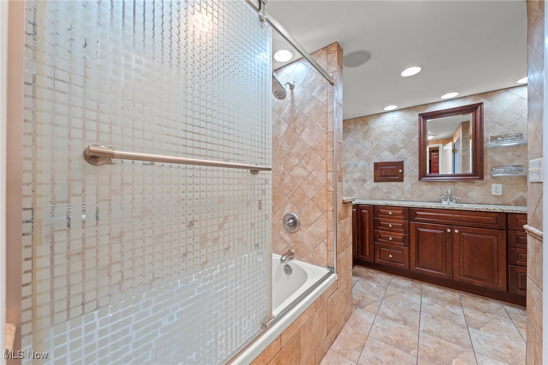 Bathroom with glass-enclosed tub and shower, beige tile, and dark wood vanity.