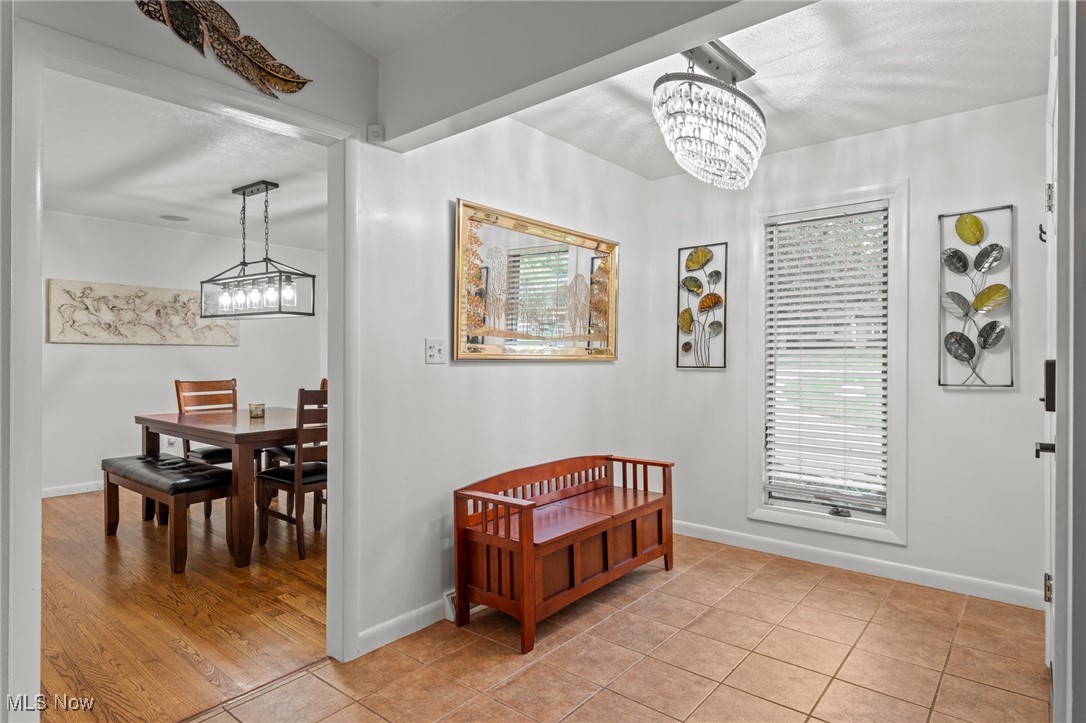 Tiled entryway with a wooden bench and chandelier, opening onto a dining room.