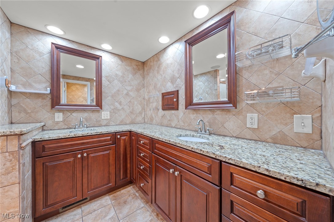 Bathroom vanity with two sinks, granite countertops, dark wood cabinets, and beige tile.