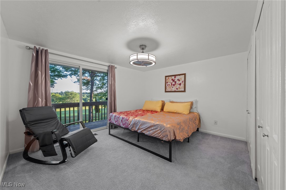 Bedroom with colorful bedding, a black reclining chair, and sliding doors to a tree-lined balcony.