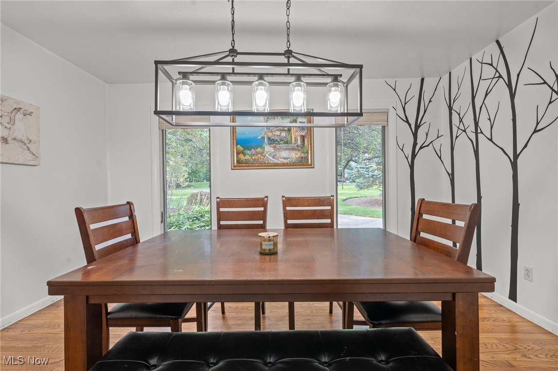 Dining room with a large wooden table, branch mural, and windows overlooking the garden.