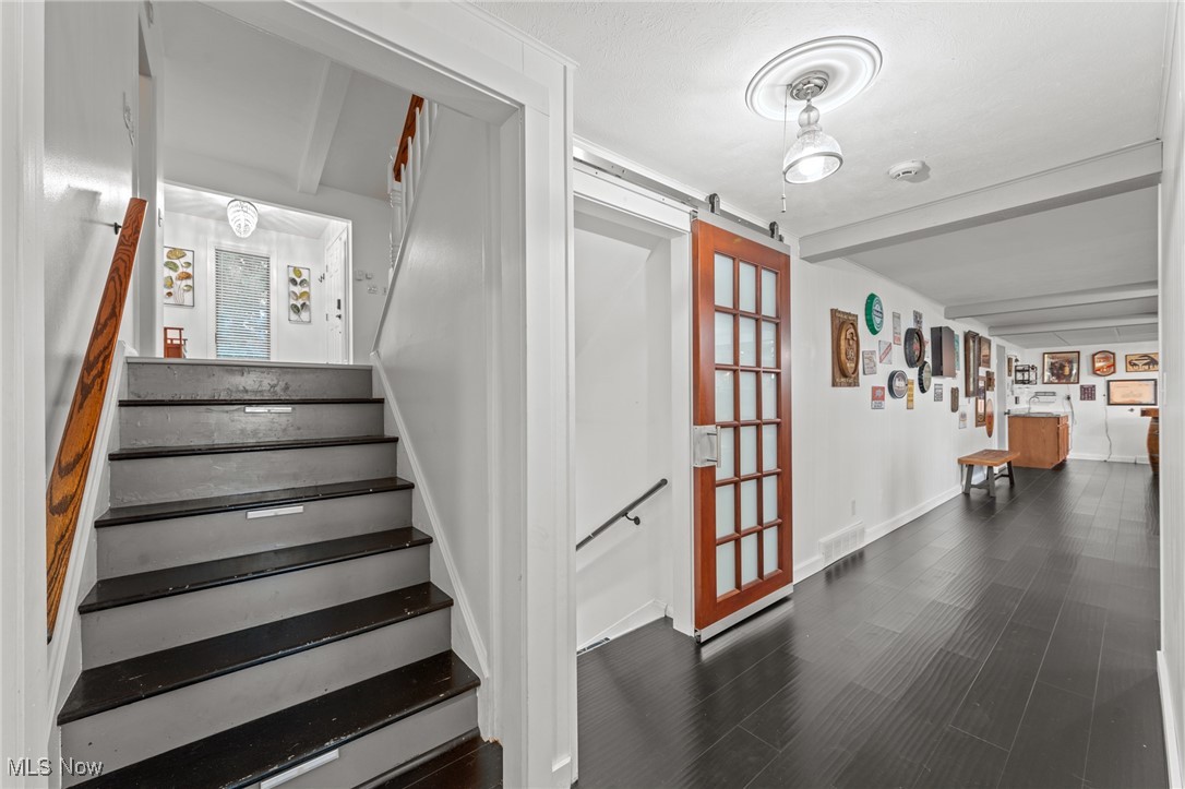 Hallway with a dark-tread staircase, wood-framed glass door, and dark flooring.