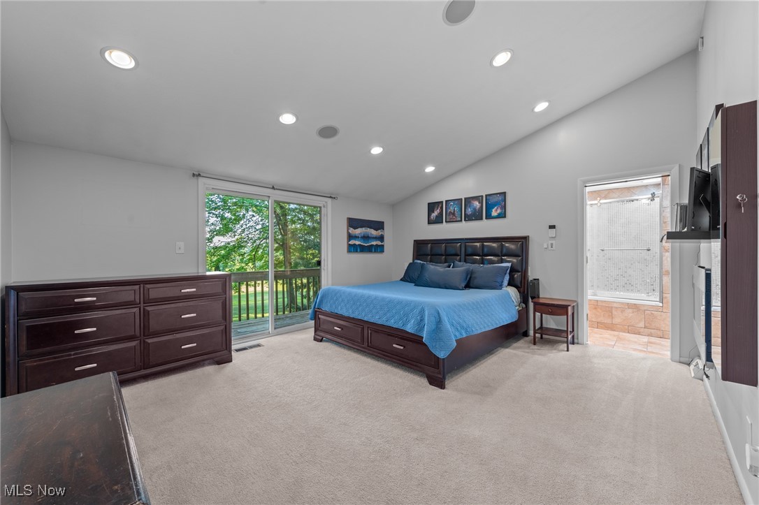 Bedroom with a blue-covered bed, dark wood dressers, and a sliding door to a leafy balcony.