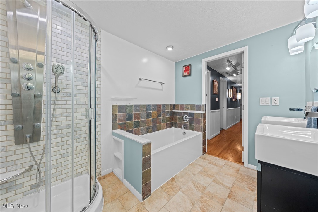Bathroom with glass-enclosed subway-tile shower, colorful tiled bathtub surround, and double vanity.