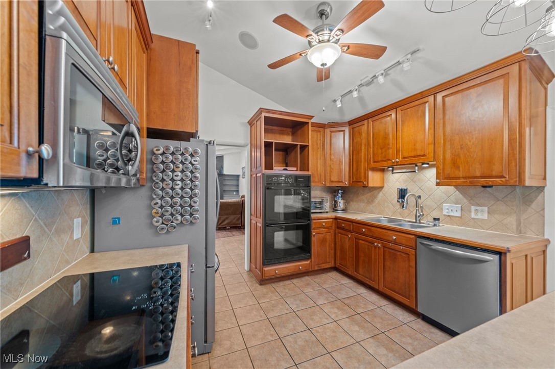 Kitchen with warm wood cabinetry, double wall oven, stainless-steel appliances, and tiled flooring.