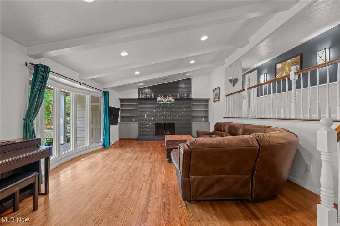 Living room with a brick fireplace, hardwood floors, and a brown leather sectional.