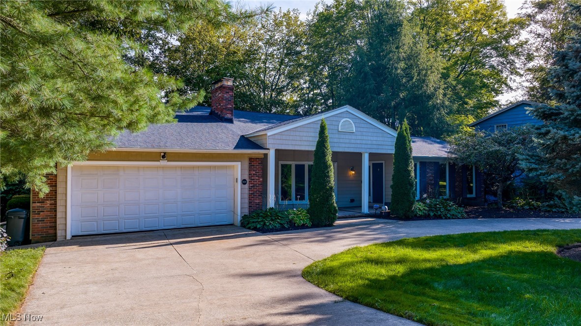 Single-story home with a two-car garage, brick accents, and mature trees framing the driveway.