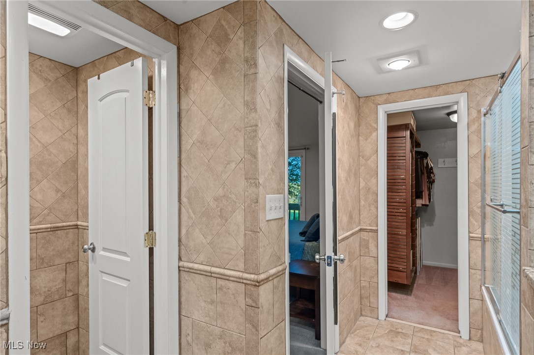 Tiled bathroom with a glass shower and an open doorway to a walk-in closet.