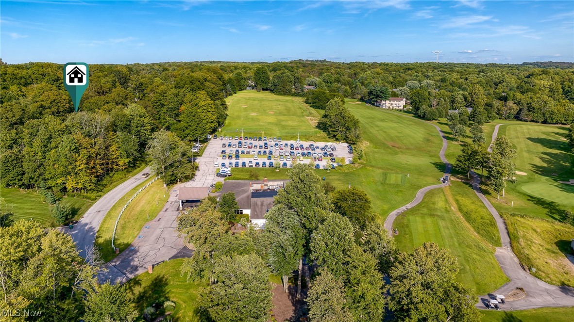 Aerial view of a golf course and wooded grounds, with a house marker above the trees.