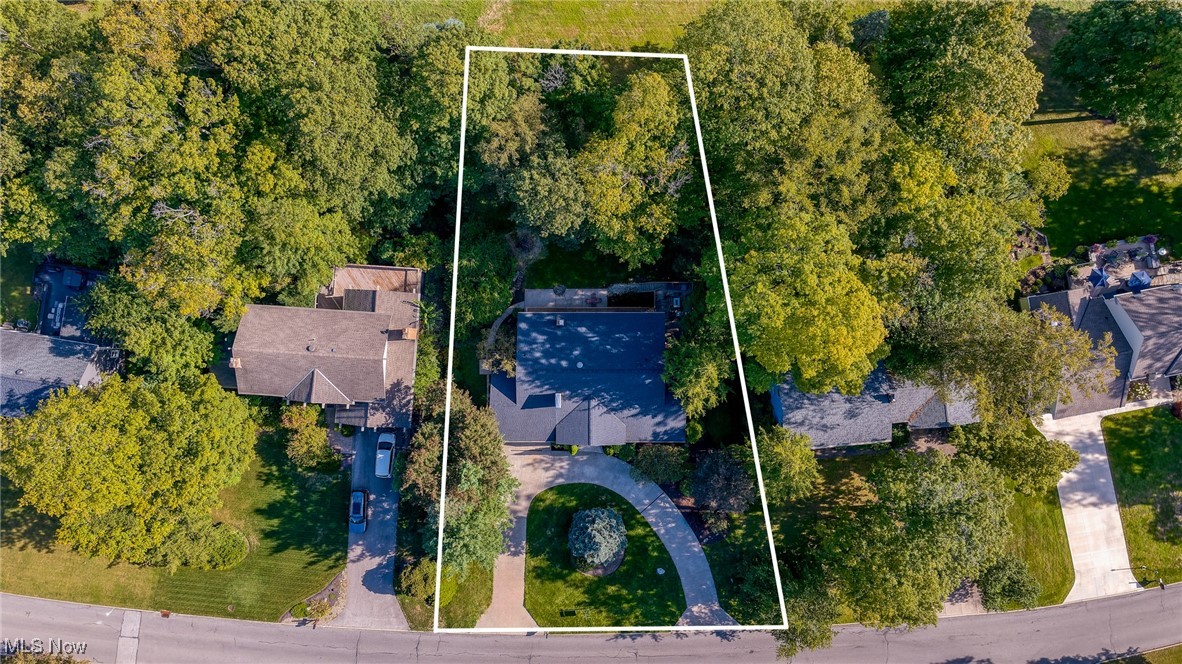Aerial view of a wooded home and curved driveway, with the property outlined in white.