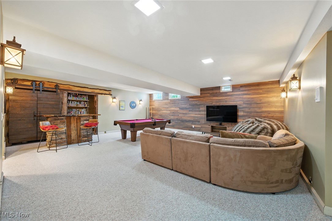 Basement recreation room with a pool table, rustic bar, and curved sectional facing a wood-paneled TV wall.