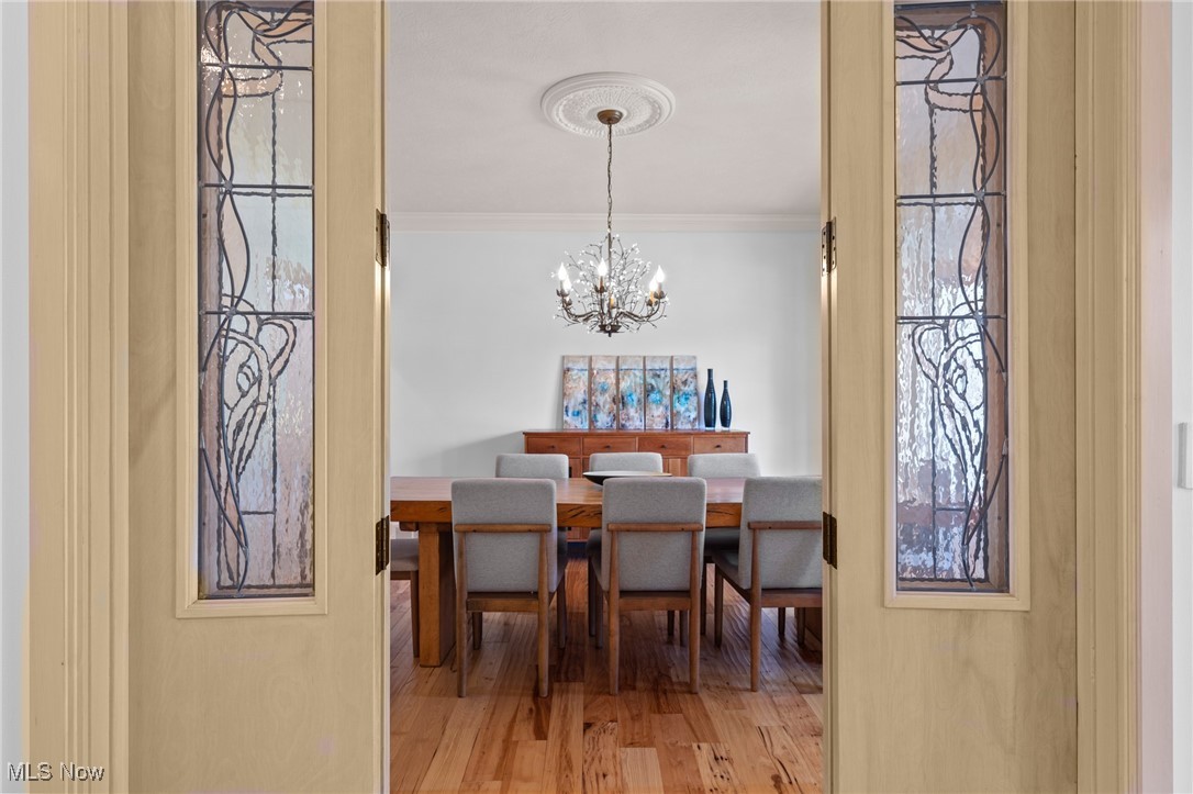 Dining room with a wooden table, gray chairs, chandelier, and stained-glass door panels.