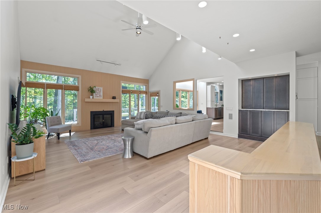 Living room with vaulted ceilings, a wood-accent fireplace wall, and large windows overlooking trees.
