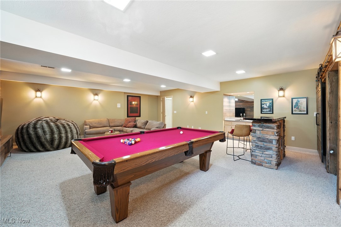 Basement game room with a magenta pool table, sofa, oversized chair, and stone-front bar.