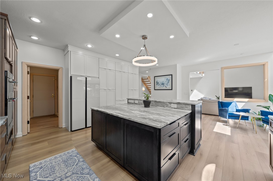 Modern kitchen with a large dark island and white cabinetry, opening to a sunlit living area.