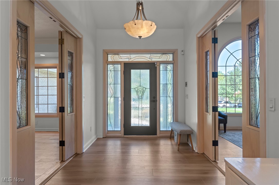 Entry foyer with a decorative glass front door, hardwood floors, and a small upholstered bench.