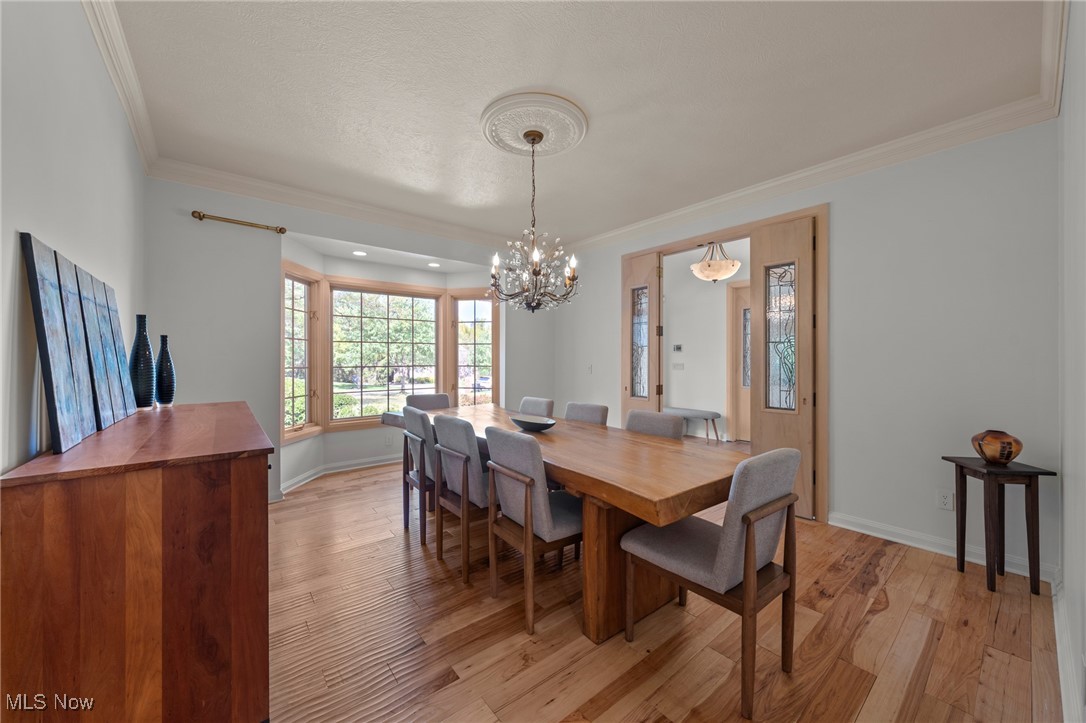 Dining room with a long wooden table, chandelier, hardwood floors, and large bay windows.