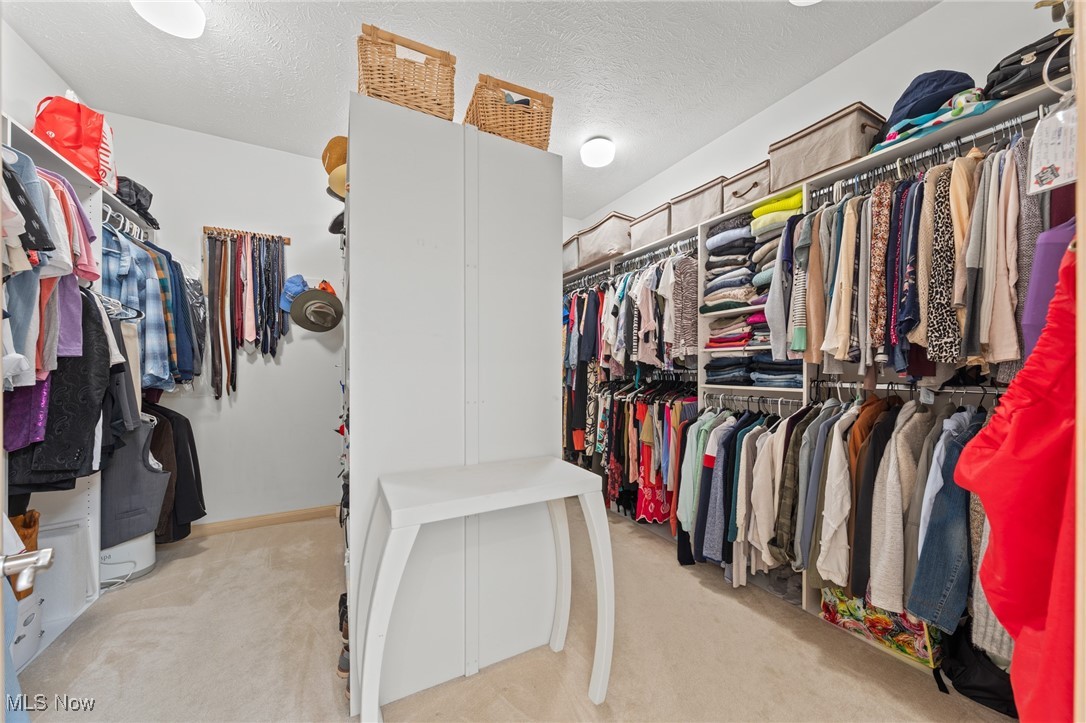 Walk-in closet with extensive hanging clothes and a tall white cabinet at the center.
