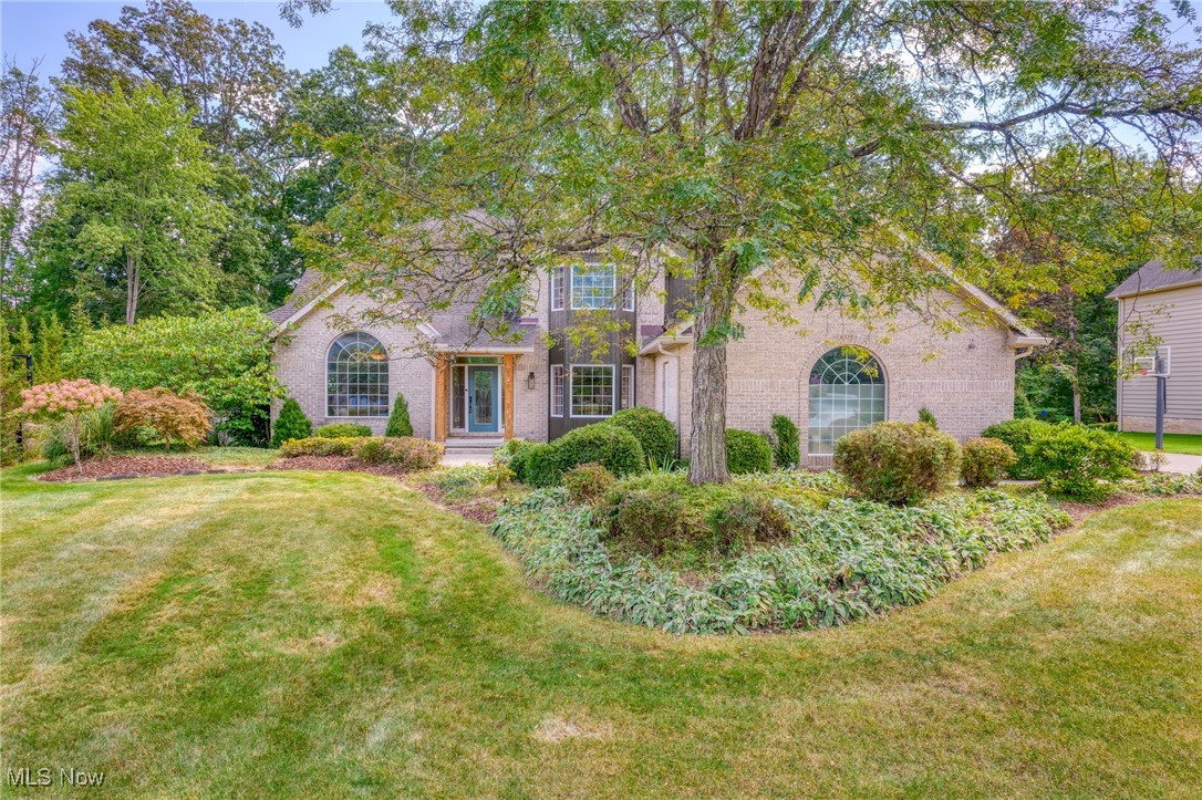Two-story brick house with arched windows, mature trees, and landscaped front garden.