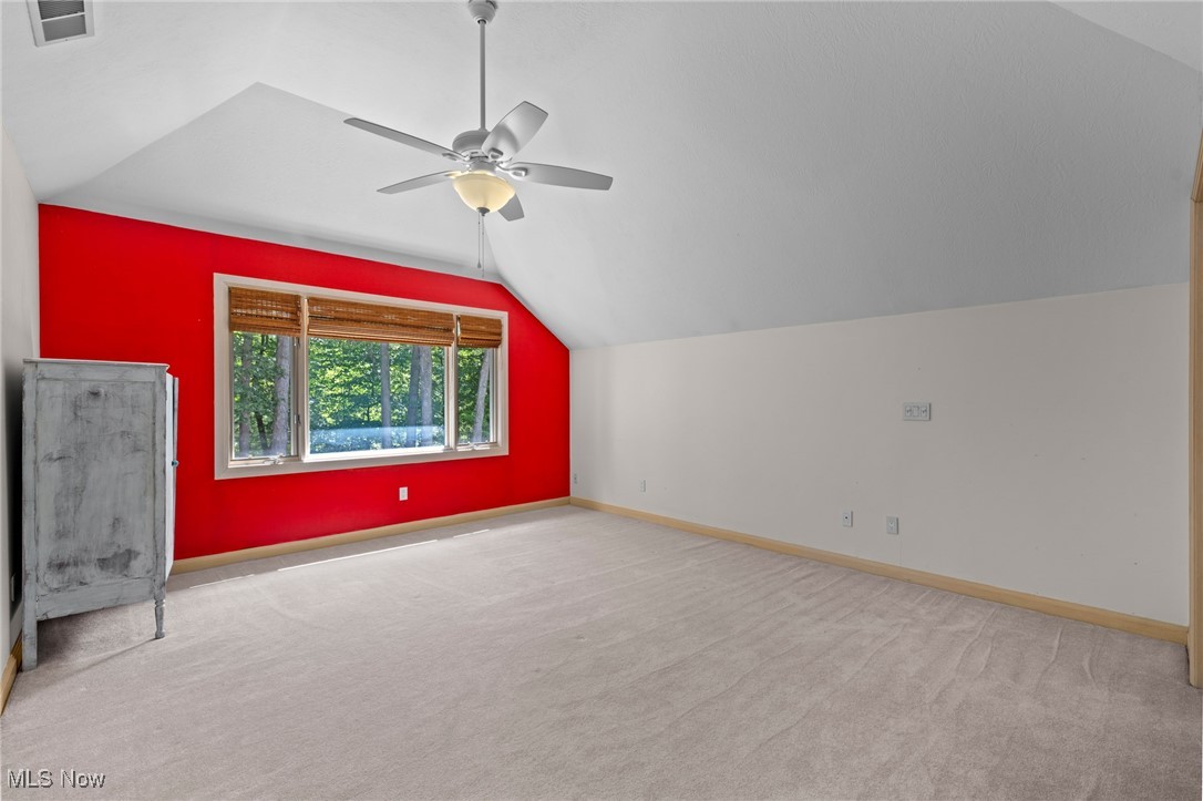Unfurnished bedroom with a red accent wall, wide window, beige carpet, and ceiling fan.