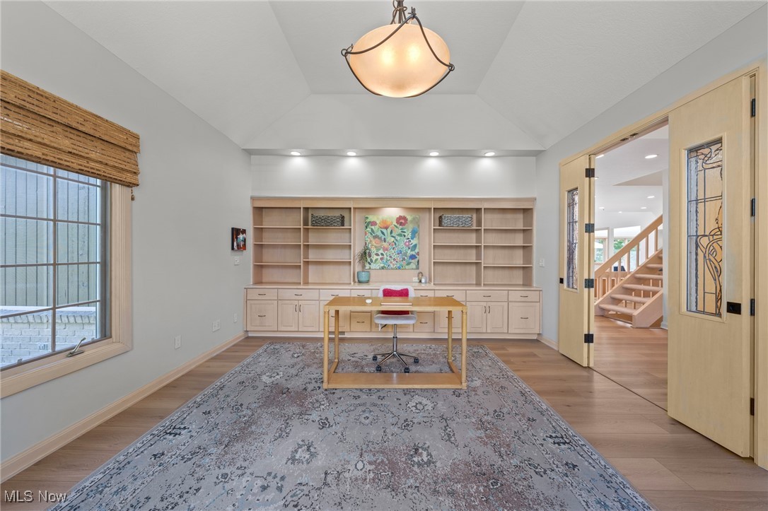 Home office with built-in shelves, a central desk, and open doors to a staircase.
