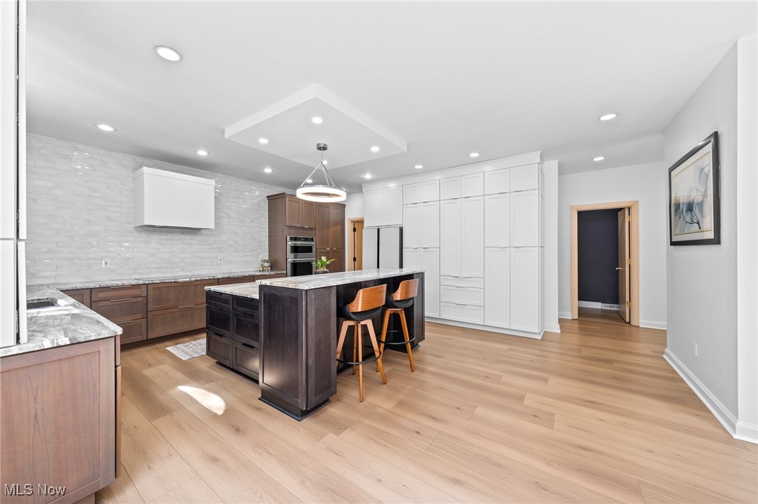 Modern kitchen with a dark wood island, two stools, white cabinetry, and light wood floors.