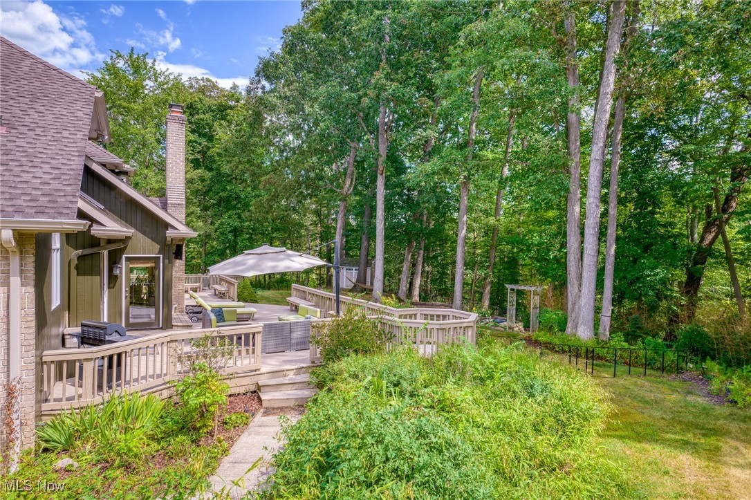 Home’s wooded backyard with a raised deck, outdoor seating, and a large patio umbrella.