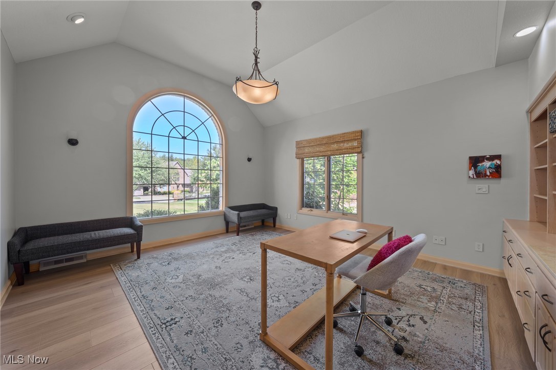 Home office with a vaulted ceiling, arched window, and built-in desk and cabinetry.