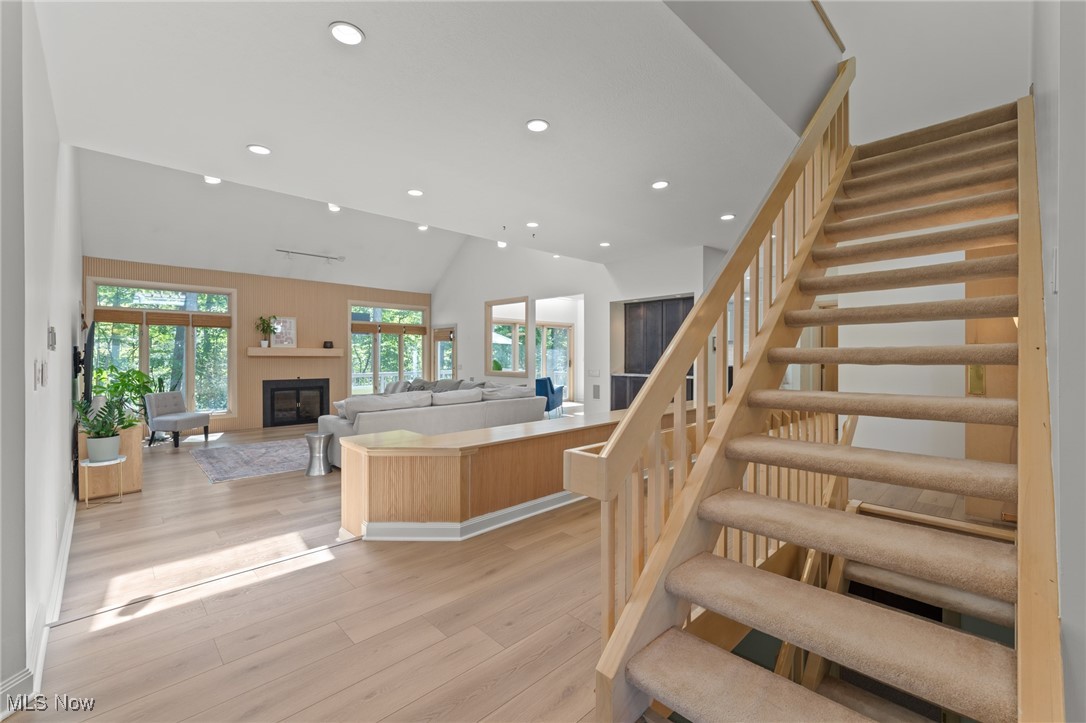 Open living room with a wood-paneled fireplace wall and a carpeted staircase with natural wood railings.