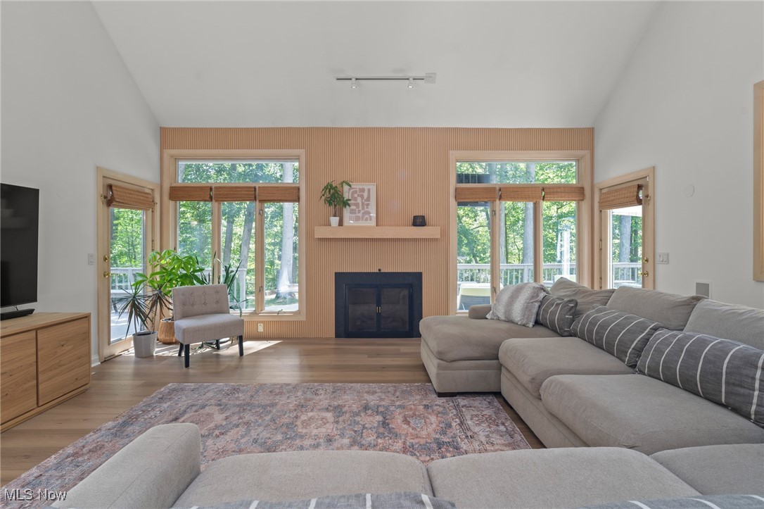 Living room with a wood-slat fireplace wall, large windows overlooking trees, and a gray sectional sofa.