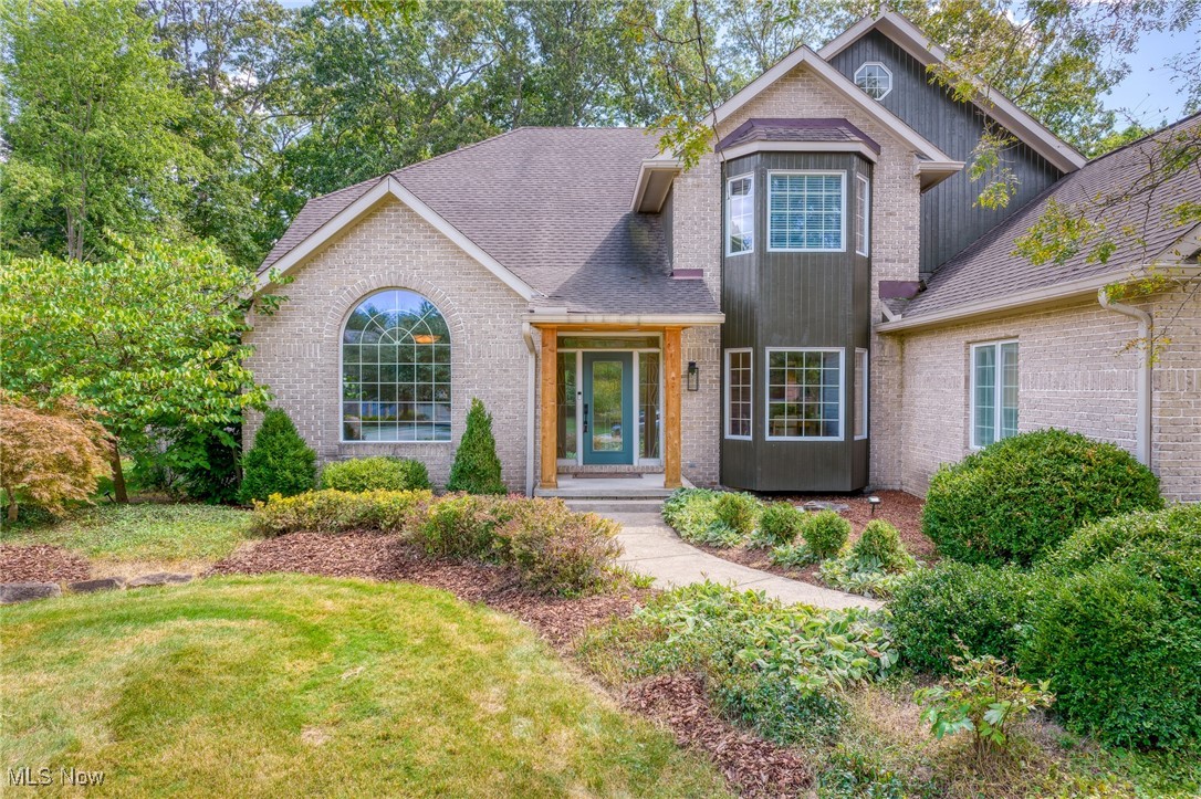 Brick home with dark siding, a covered entry, and landscaped front garden.