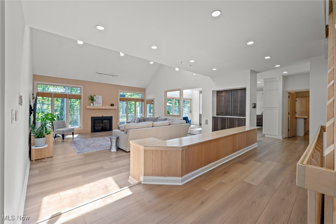 Open living room with vaulted ceiling, fireplace, large windows, and a long wood-paneled island.