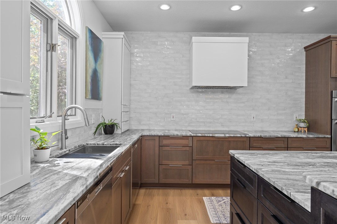 Modern kitchen with warm wood cabinets, marble counters, a large island, and windows above the sink.