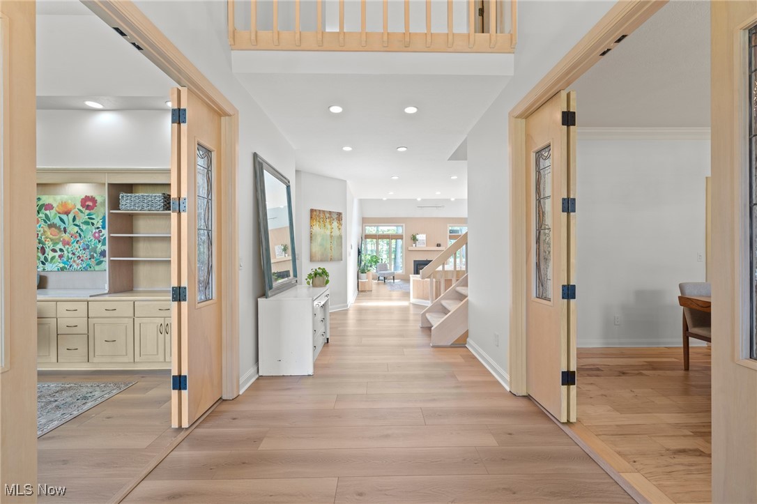 Entry hall with pale wood floors, open wood doors, built-in cabinetry, and a staircase.