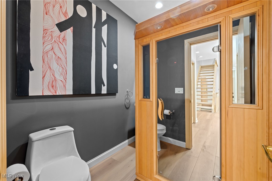 Modern bathroom with abstract wall art and a wood-framed glass enclosure beside a bright hallway.