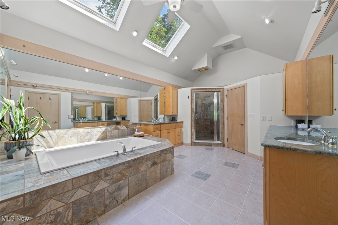Bathroom with a tiled soaking tub and glass shower beneath a vaulted ceiling with skylights.