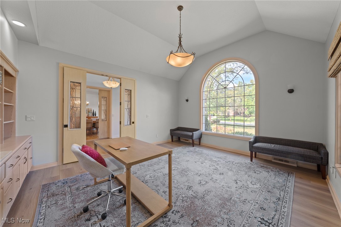Home office with a wood desk, built-in cabinetry, and a large arched window overlooking the lawn.