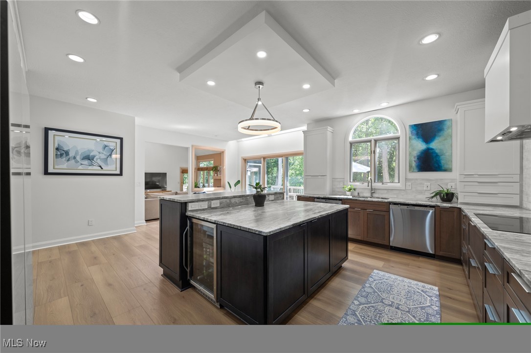 Kitchen with a large dark-wood island, gray stone counters, white cabinets, and an arched window overlooking trees.