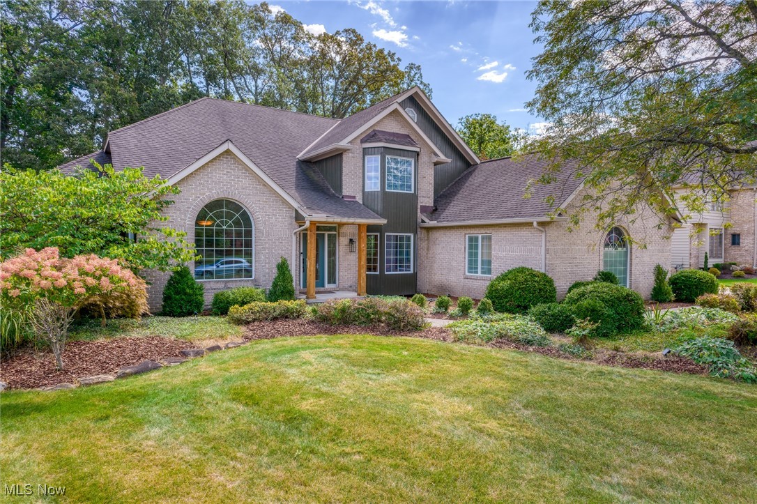 Brick home with arched windows, a covered entrance, landscaped shrubs, and a broad front lawn.