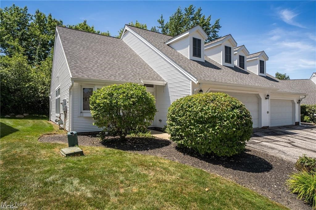 White-sided home with multiple dormers, attached garages, and a landscaped front lawn.