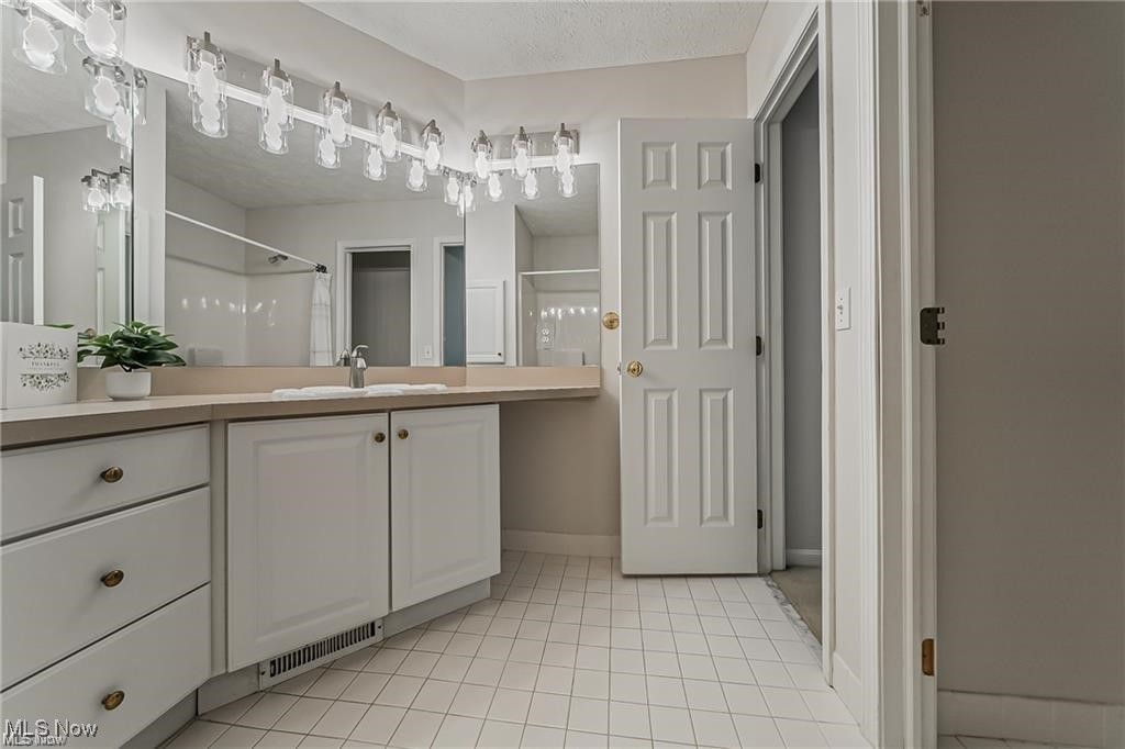 Bathroom with a long white vanity, large mirror, and tiled floor.