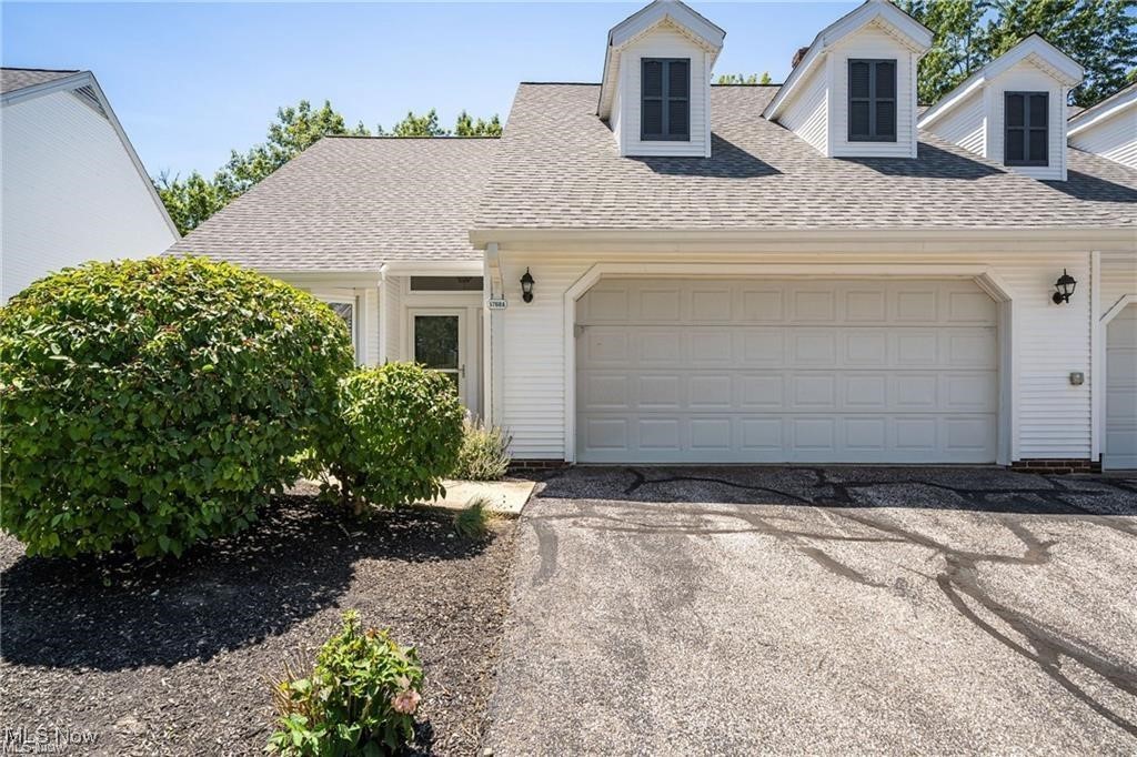 White-sided home with a double garage, three dormers, and landscaped shrubs beside the driveway.