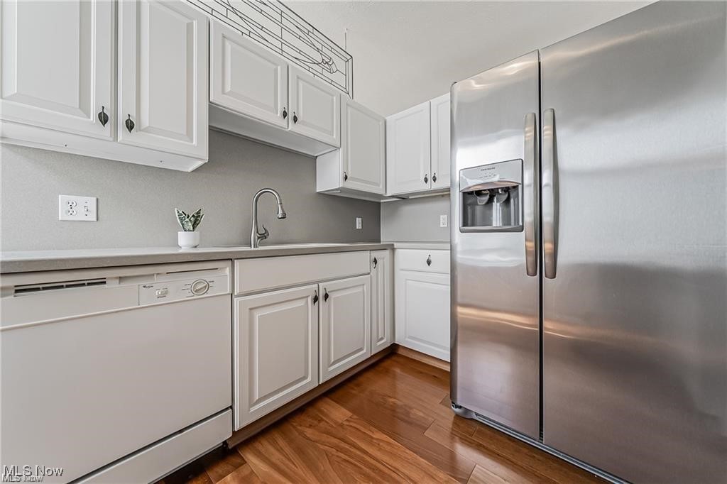 Kitchen with white cabinets, stainless steel appliances, and warm-toned hardwood flooring.