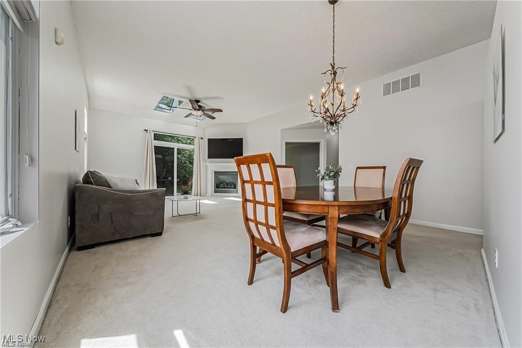 Open-plan dining and living room with a wood table, chandelier, fireplace, and sliding glass doors.