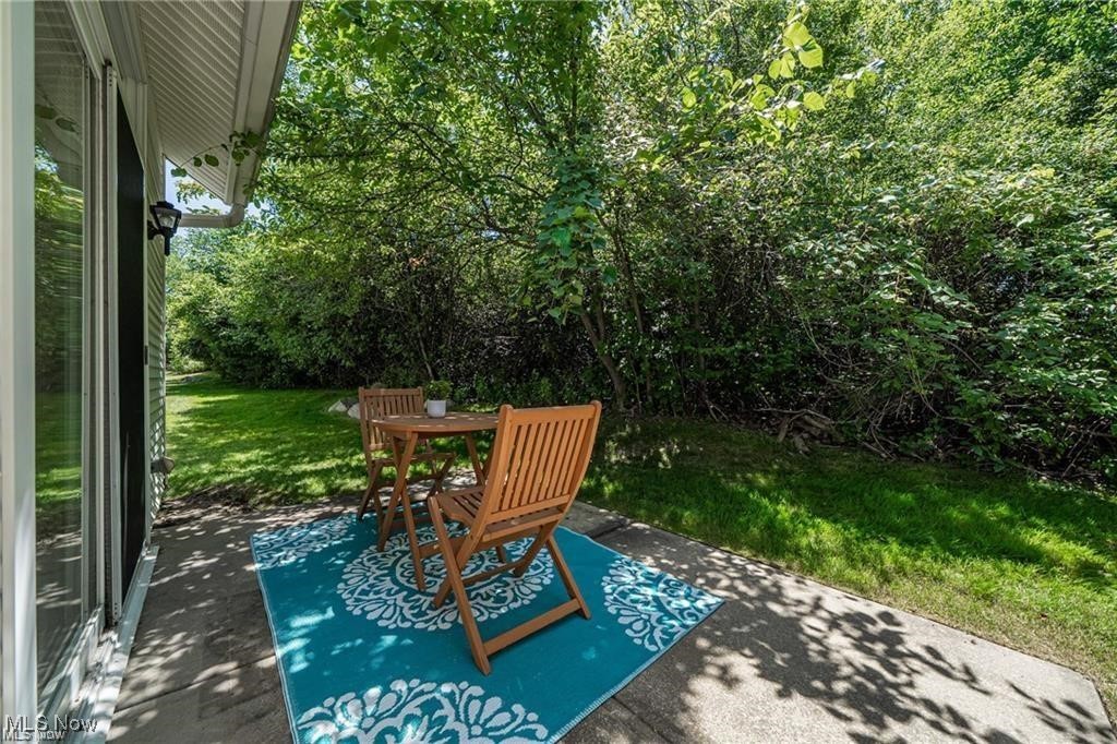 Patio with wooden chairs on a turquoise patterned rug, shaded by leafy trees.