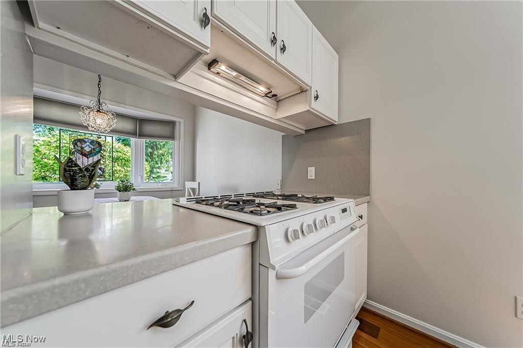 Kitchen with white cabinetry, a gas range, light countertops, and a window overlooking leafy trees.