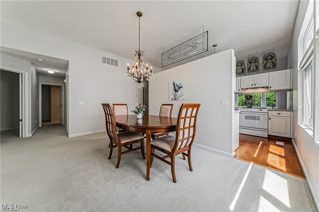 Dining room with a round wooden table, chandelier, and view into the adjoining kitchen.