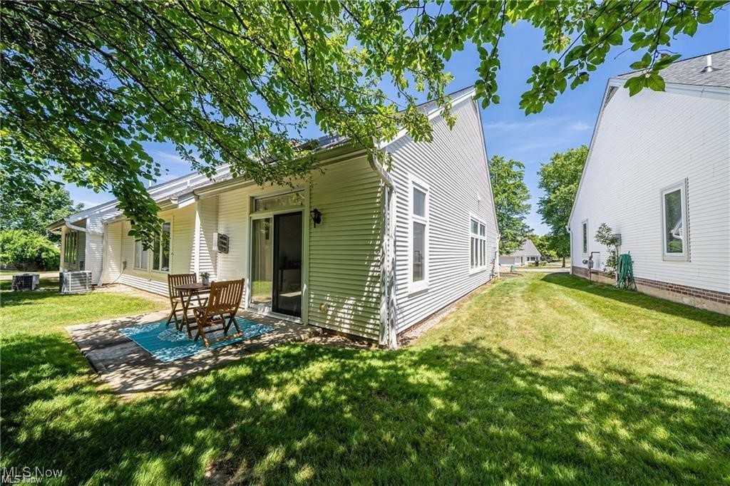 Home’s rear patio with a wooden dining set beside a broad green lawn.